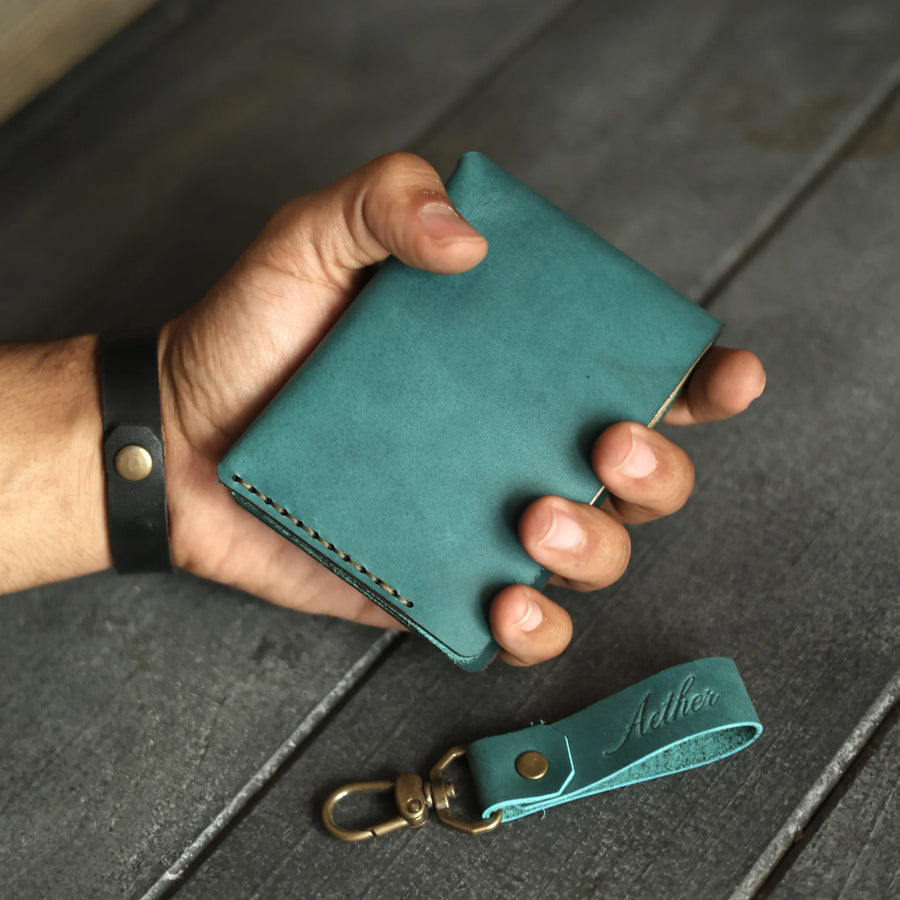Aether blue leather bifold wallet held closed in hand with matching keychain